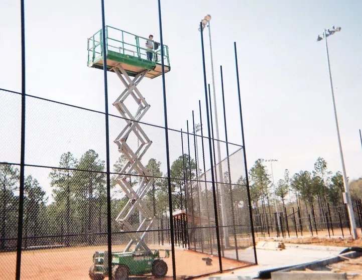 A man on a scissor lift is working on a fence