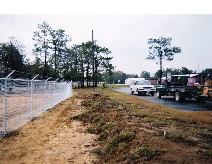 A white van is parked on the side of the road next to a fence