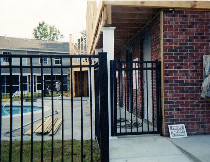 A black fence surrounds a brick building with a pool in the background