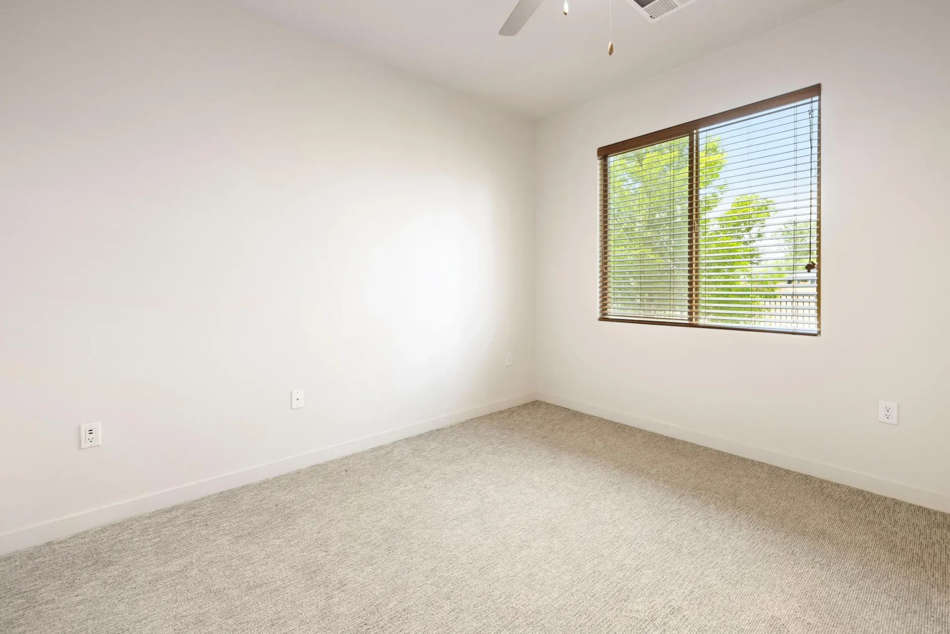 Empty beige-carpeted bedroom with a window and horizontal blinds.