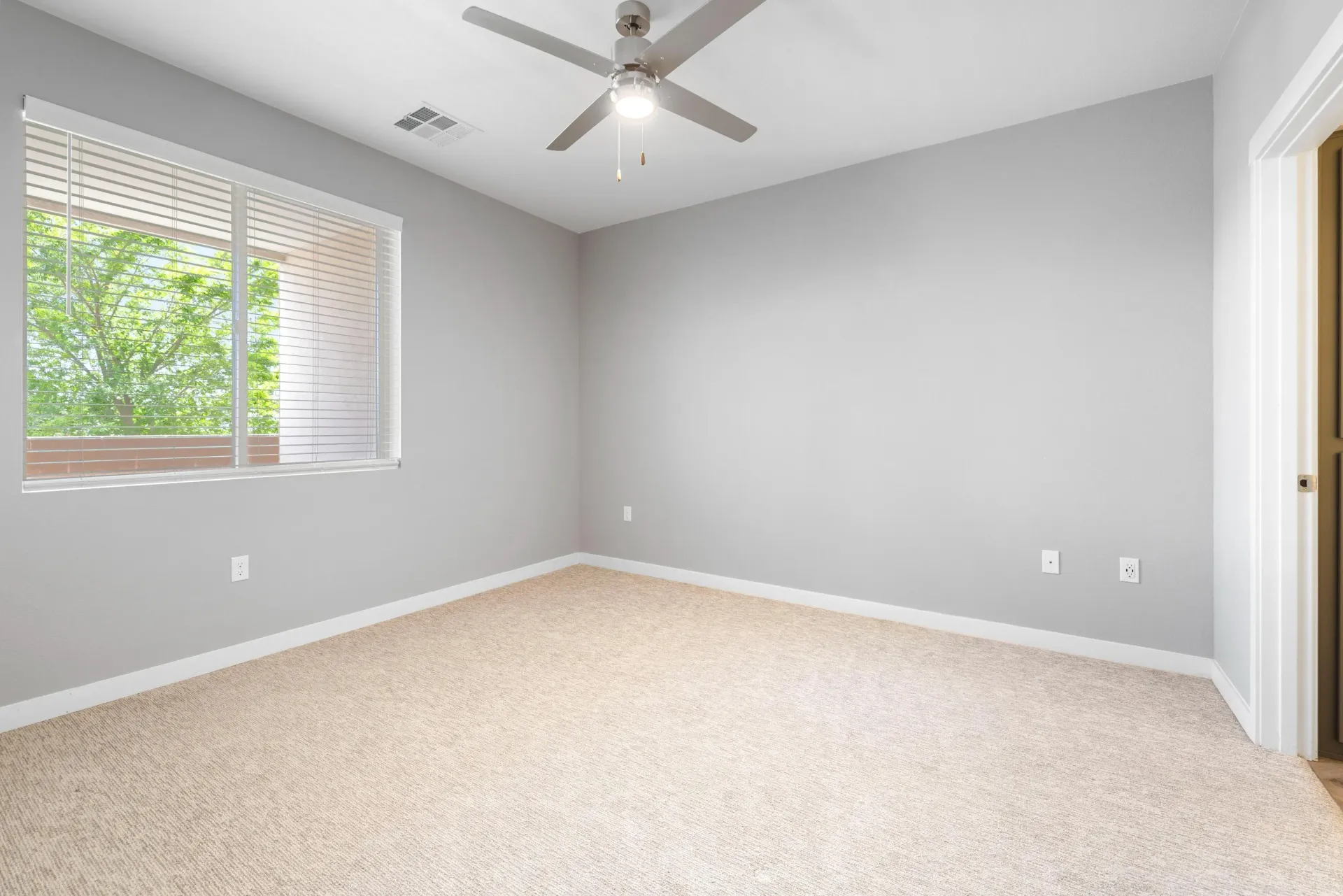 Empty gray bedroom with a window, beige carpet, and a ceiling fan.