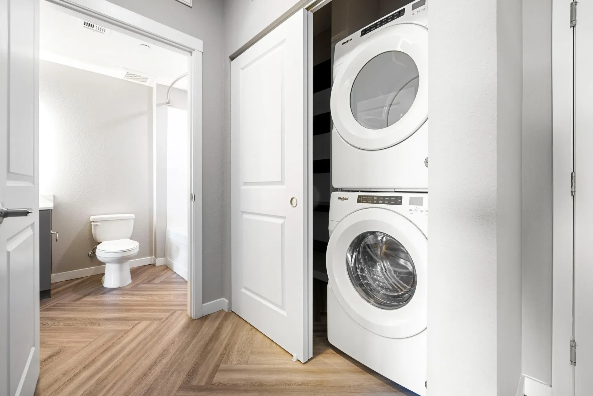 Stacked washer and dryer in a laundry closet beside a bathroom in an apartment.