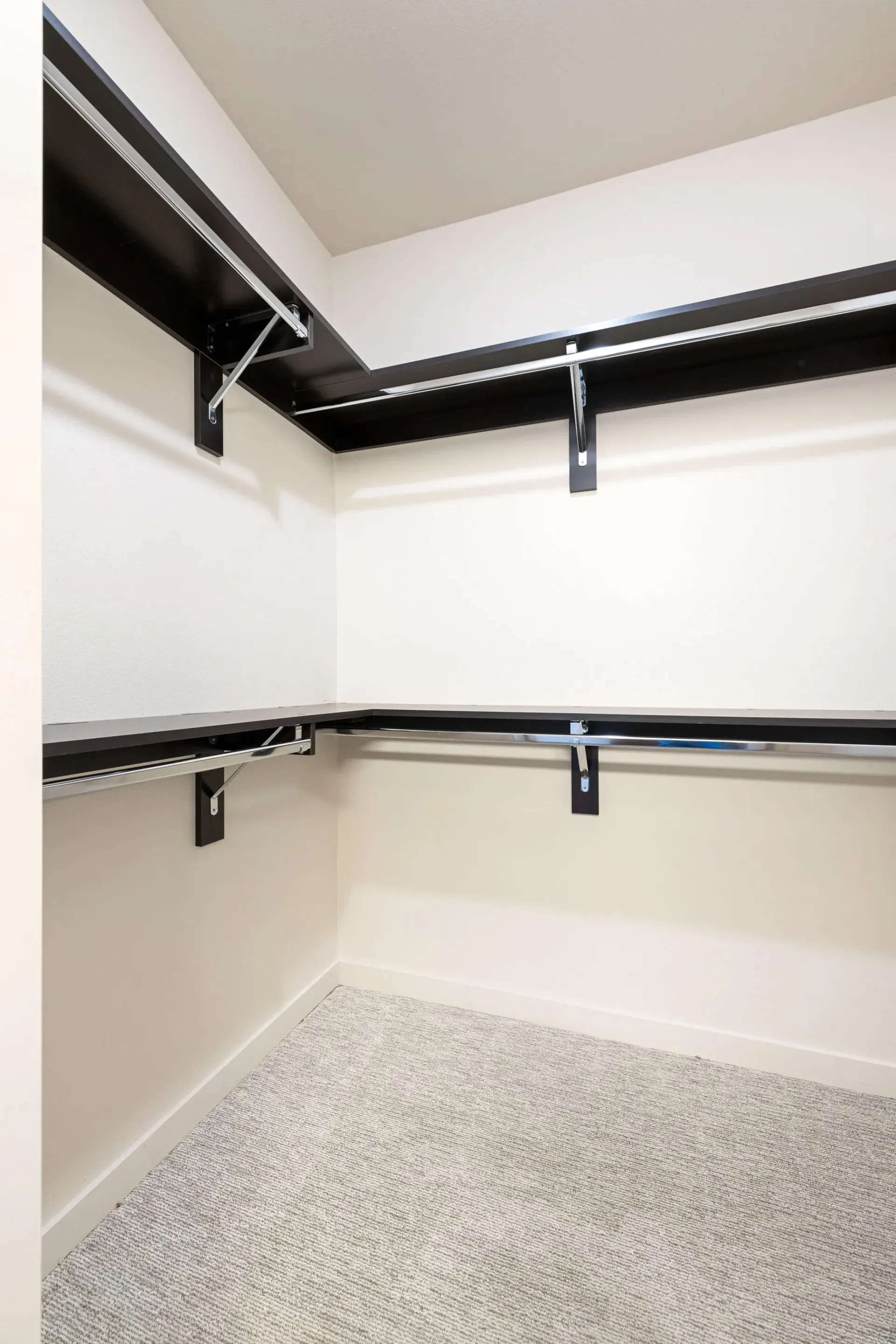 Walk-in closet with white walls, black shelves, and chrome hanging rods.