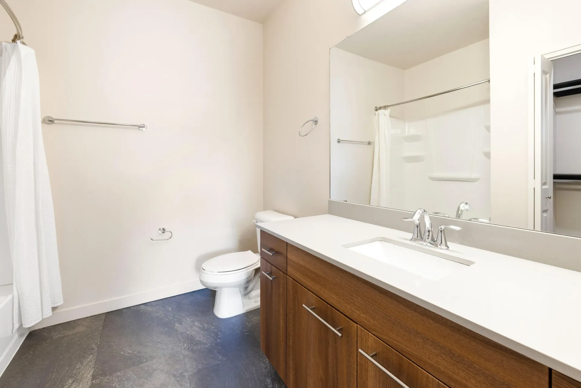Bathroom with a white countertop, wood vanity, large mirror, toilet, and shower curtain.