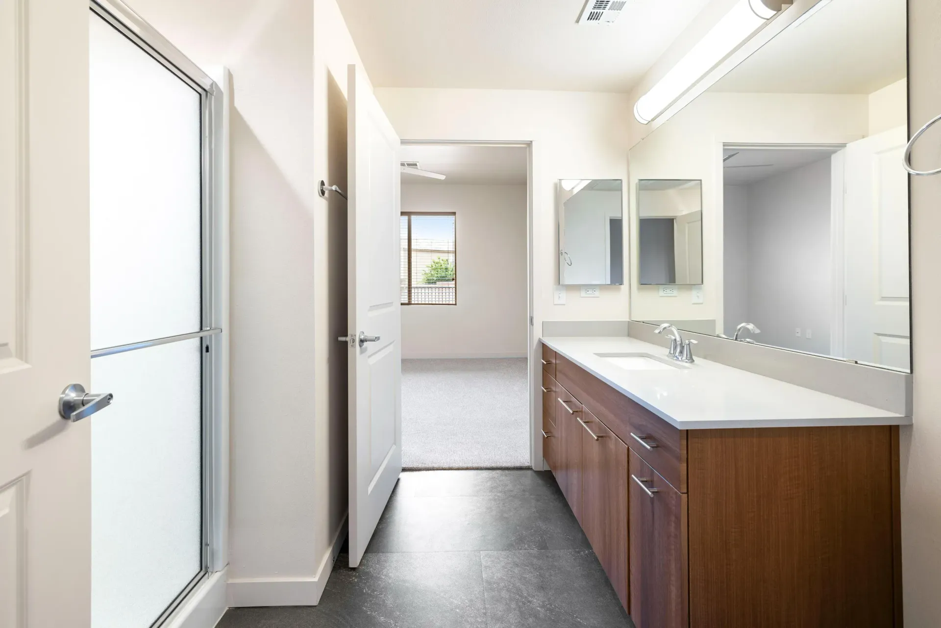Bright apartment bathroom with a single-sink vanity, large mirrors, and a frosted glass shower door.