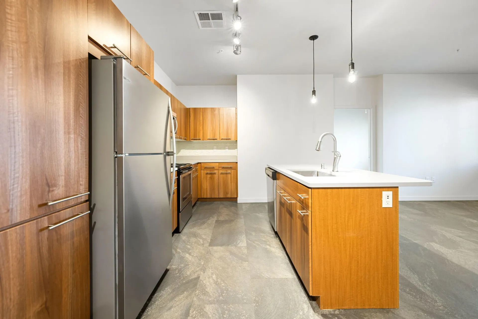 Modern apartment kitchen with wood cabinets, stainless steel fridge, and island.