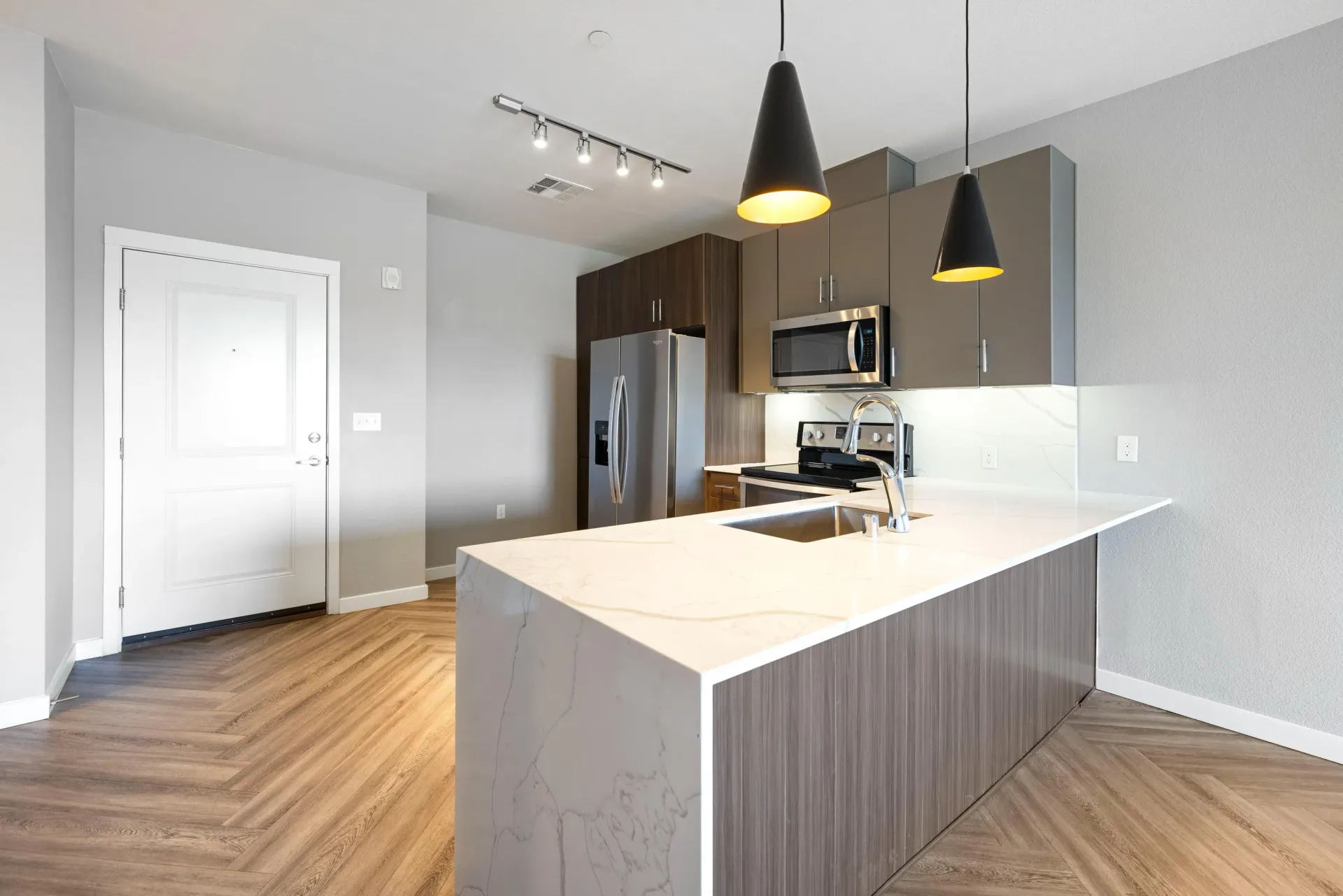 Interior view of a modern apartment kitchen with an island, stainless-steel appliances, and pendant lights.