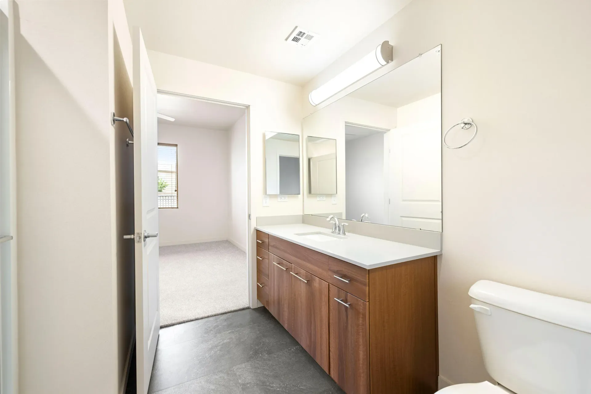 Bathroom with a wood-tone single-sink vanity, white countertop, large mirror, and toilet.