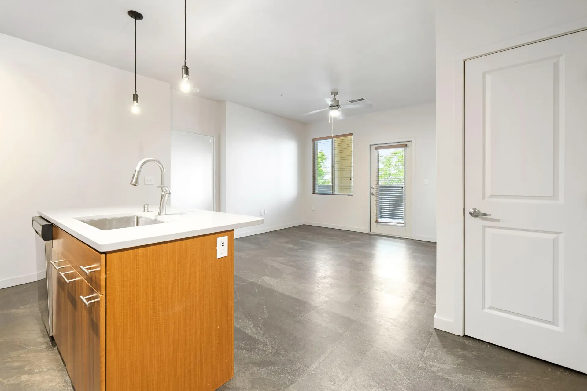 Open-concept kitchen with island, sink, and modern faucet; white counters and gray tile floor.