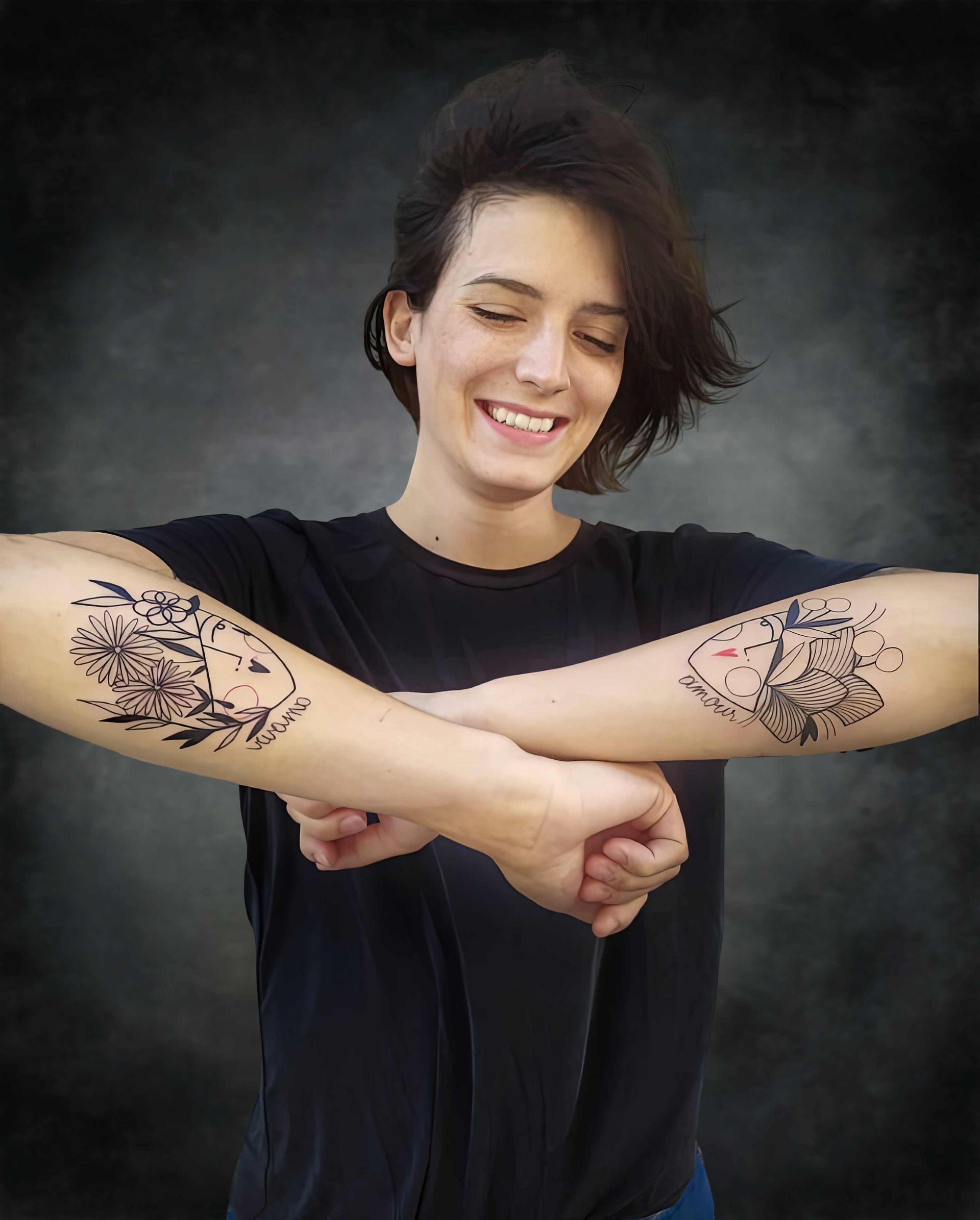 Une femme avec deux tatouages ​​​​sur les bras sourit.