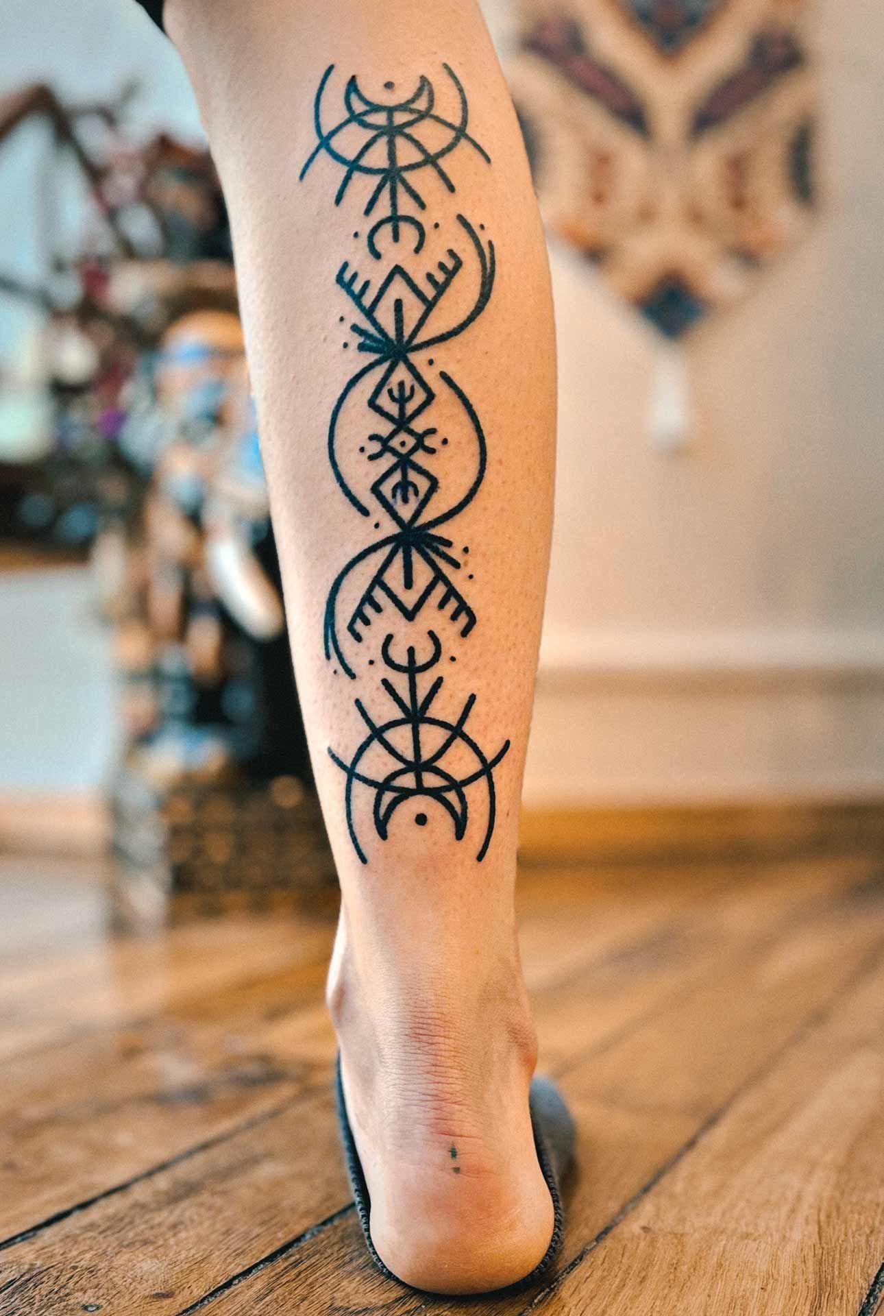 Une personne avec un tatouage sur la jambe se tient debout sur un plancher en bois.