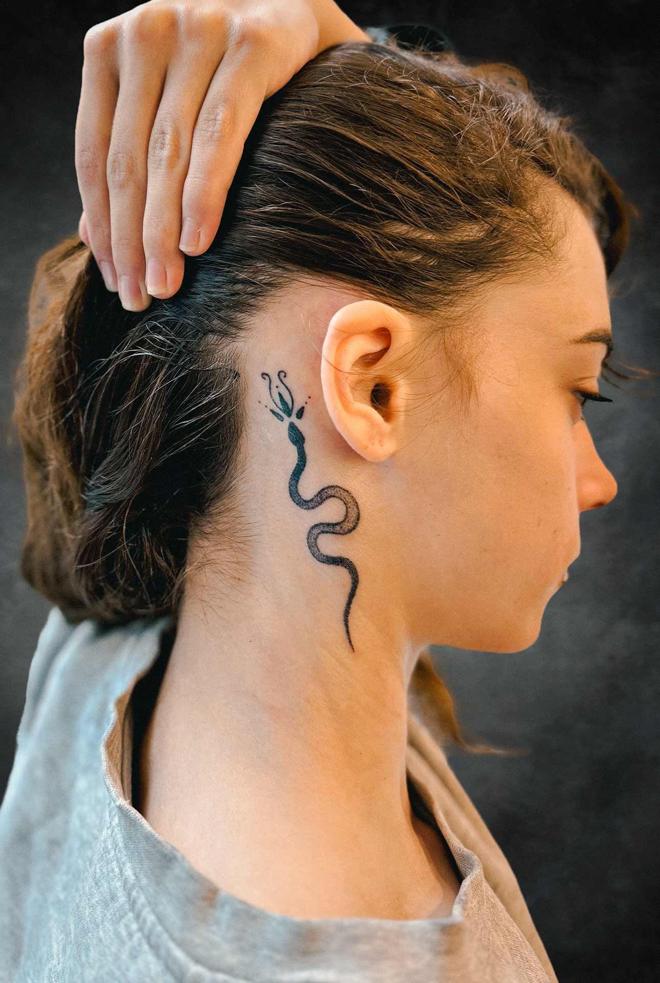Une femme a un tatouage de serpent sur son cou derrière son oreille.