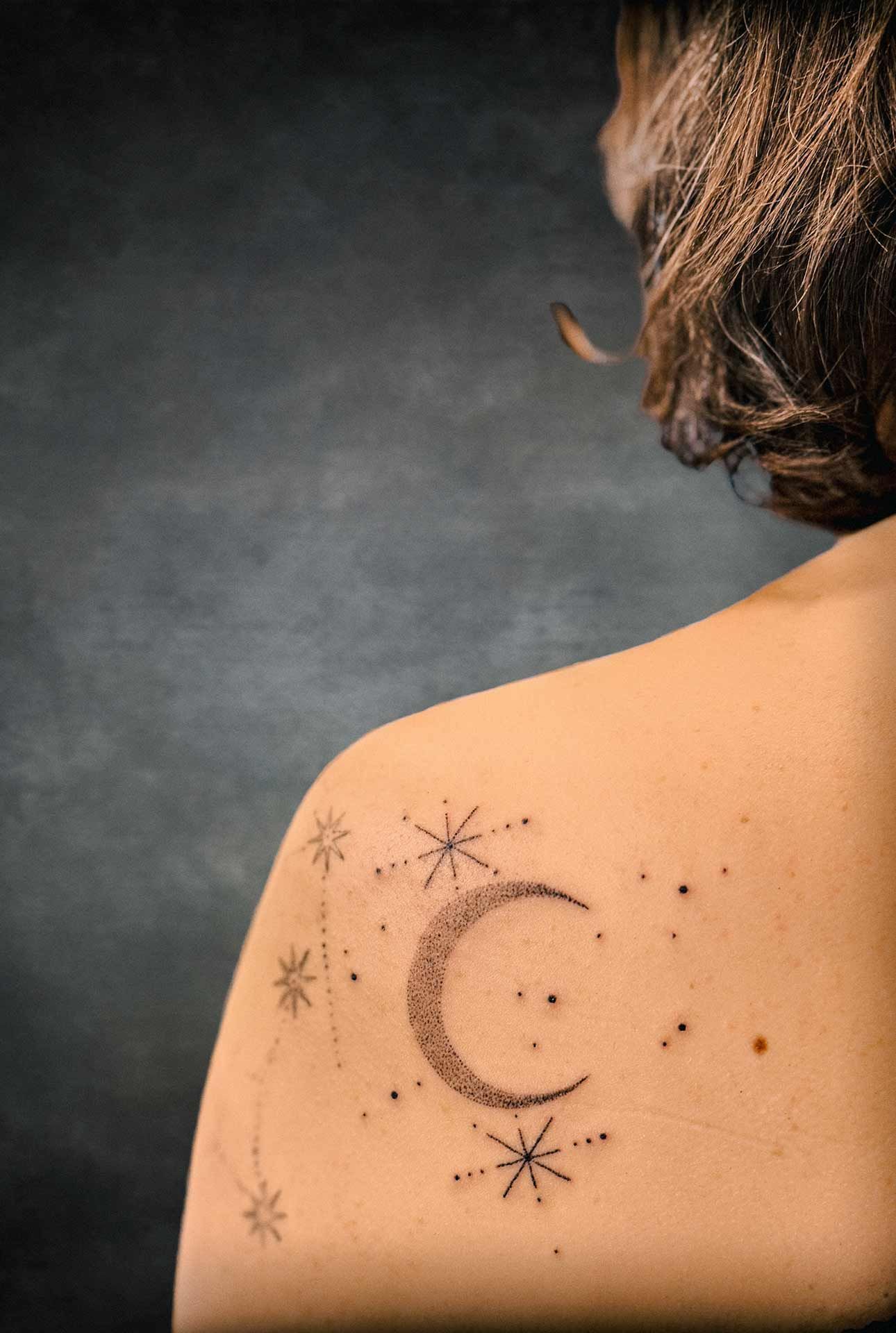 Une femme a un tatouage d'un croissant de lune et d'étoiles sur son épaule.