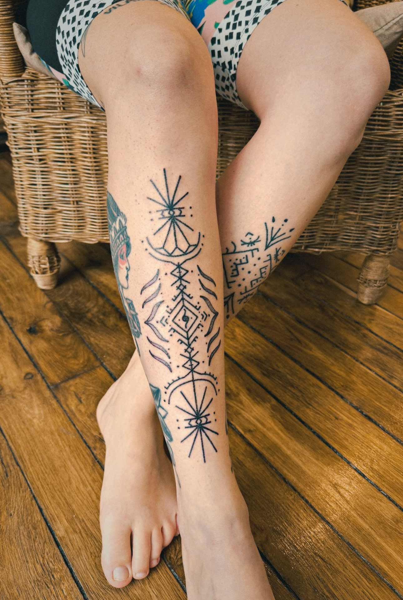 Une femme avec un tatouage sur la jambe est assise sur une chaise.