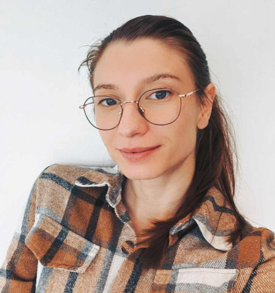 Une femme portant des lunettes et une chemise à carreaux prend un selfie.