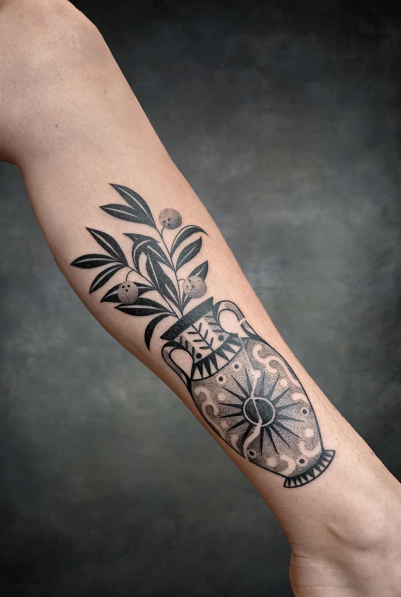 Un tatouage noir et blanc d'un vase avec des fleurs dedans sur l'avant-bras d'une personne.