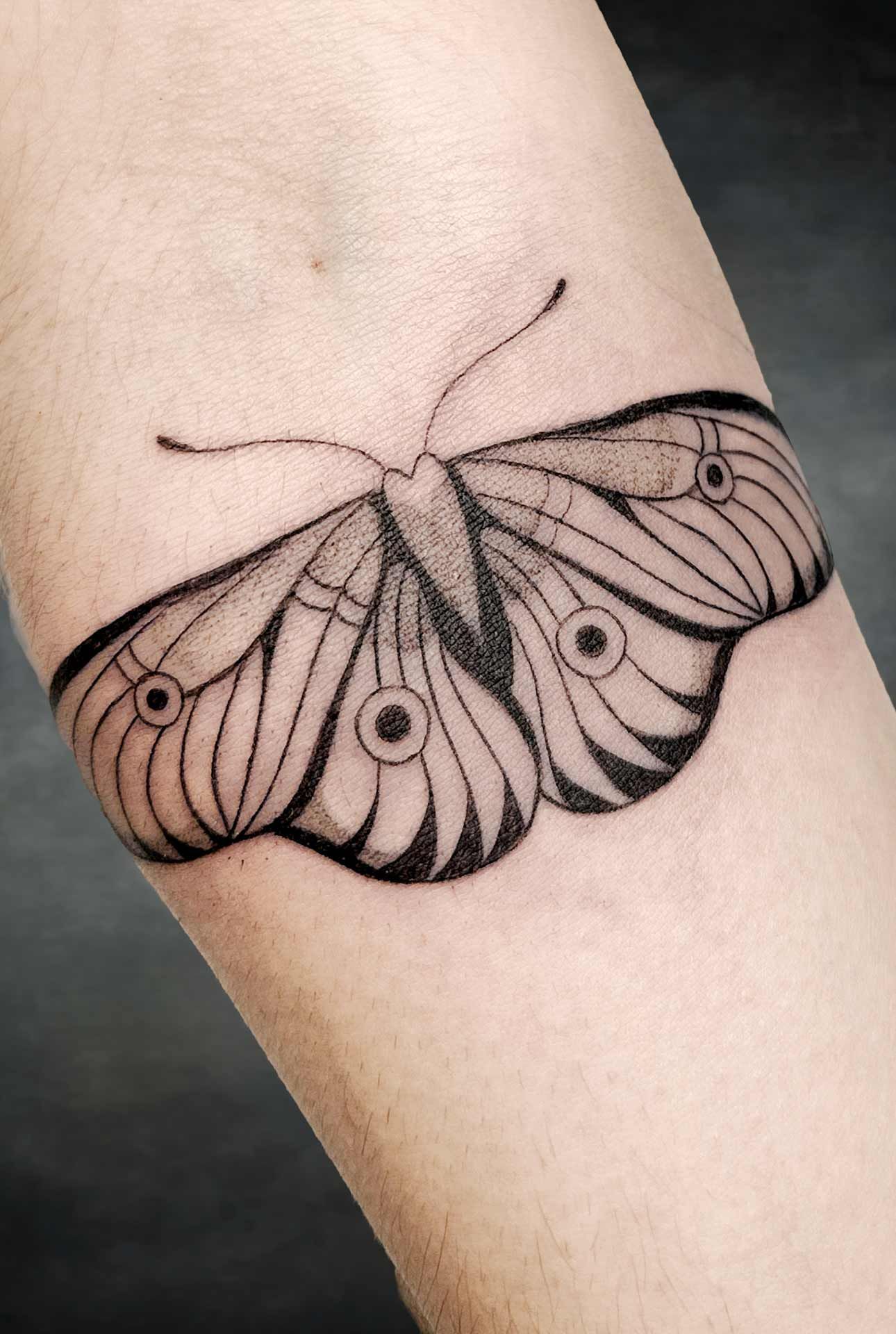Un tatouage noir et blanc d'un papillon de nuit sur l'avant-bras d'une personne.