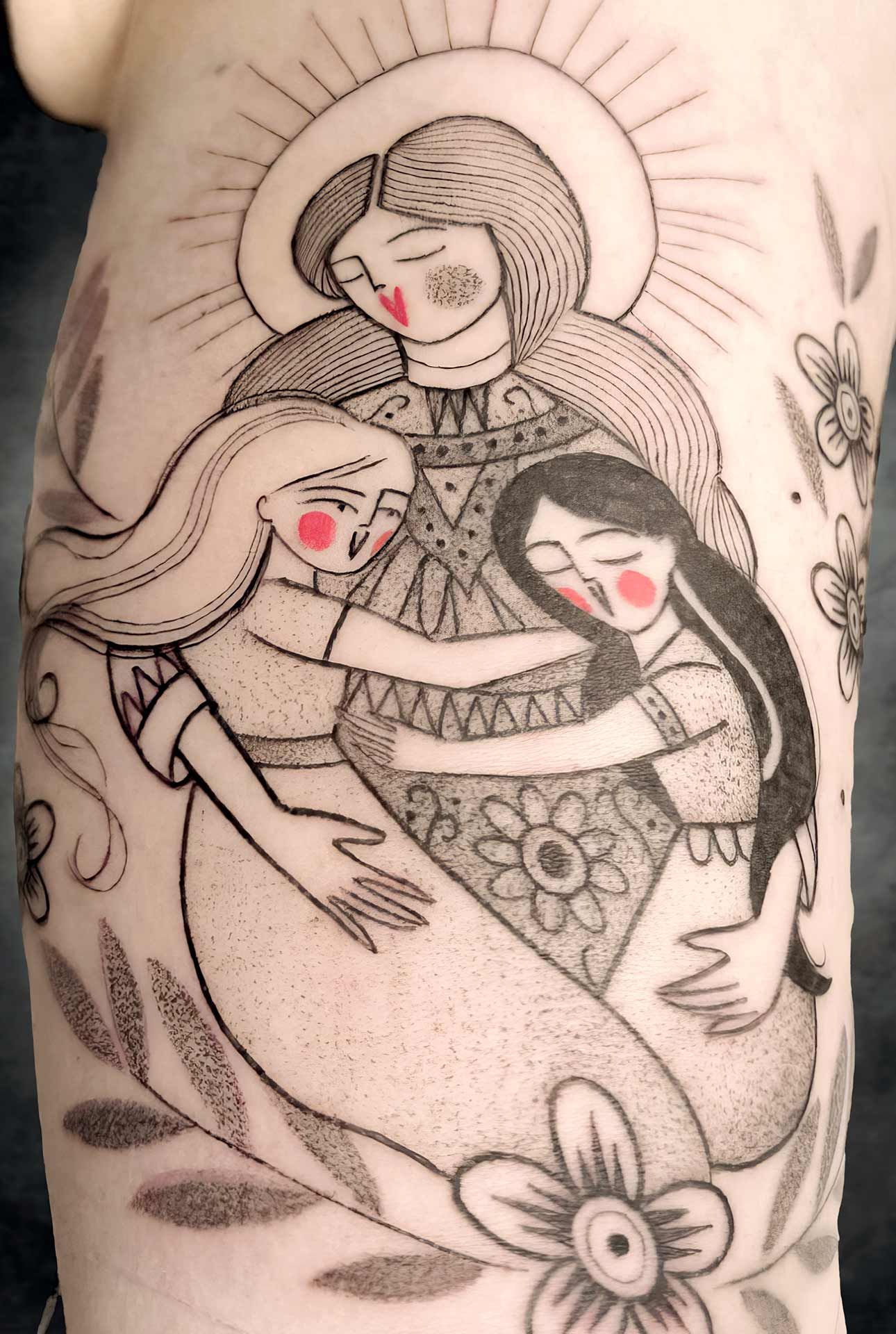 Un tatouage de trois femmes s'embrassant sur le bras d'une personne