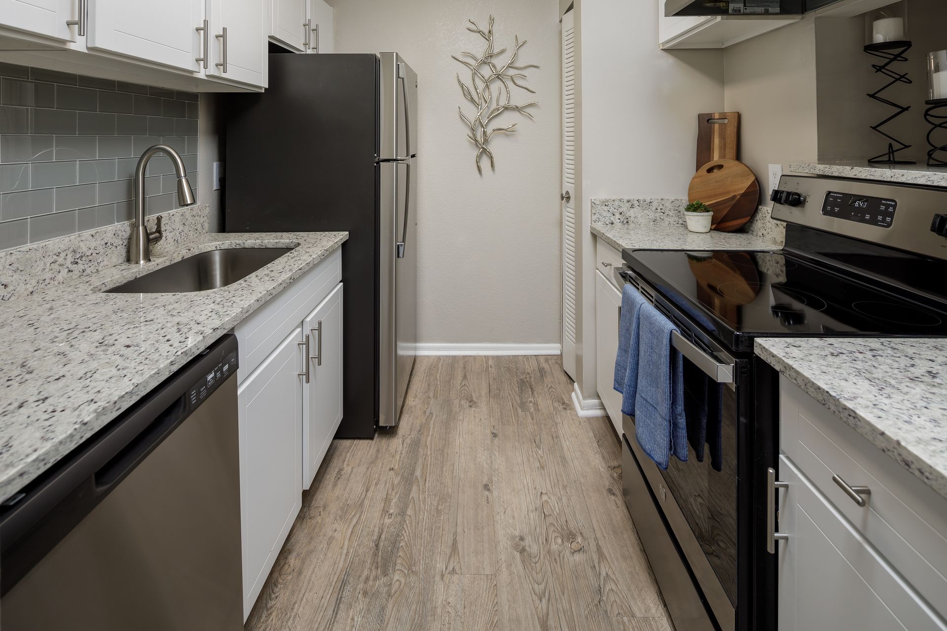 Galley kitchen with stainless steel appliances, granite counters, gray tile backsplash, and wood-look flooring.