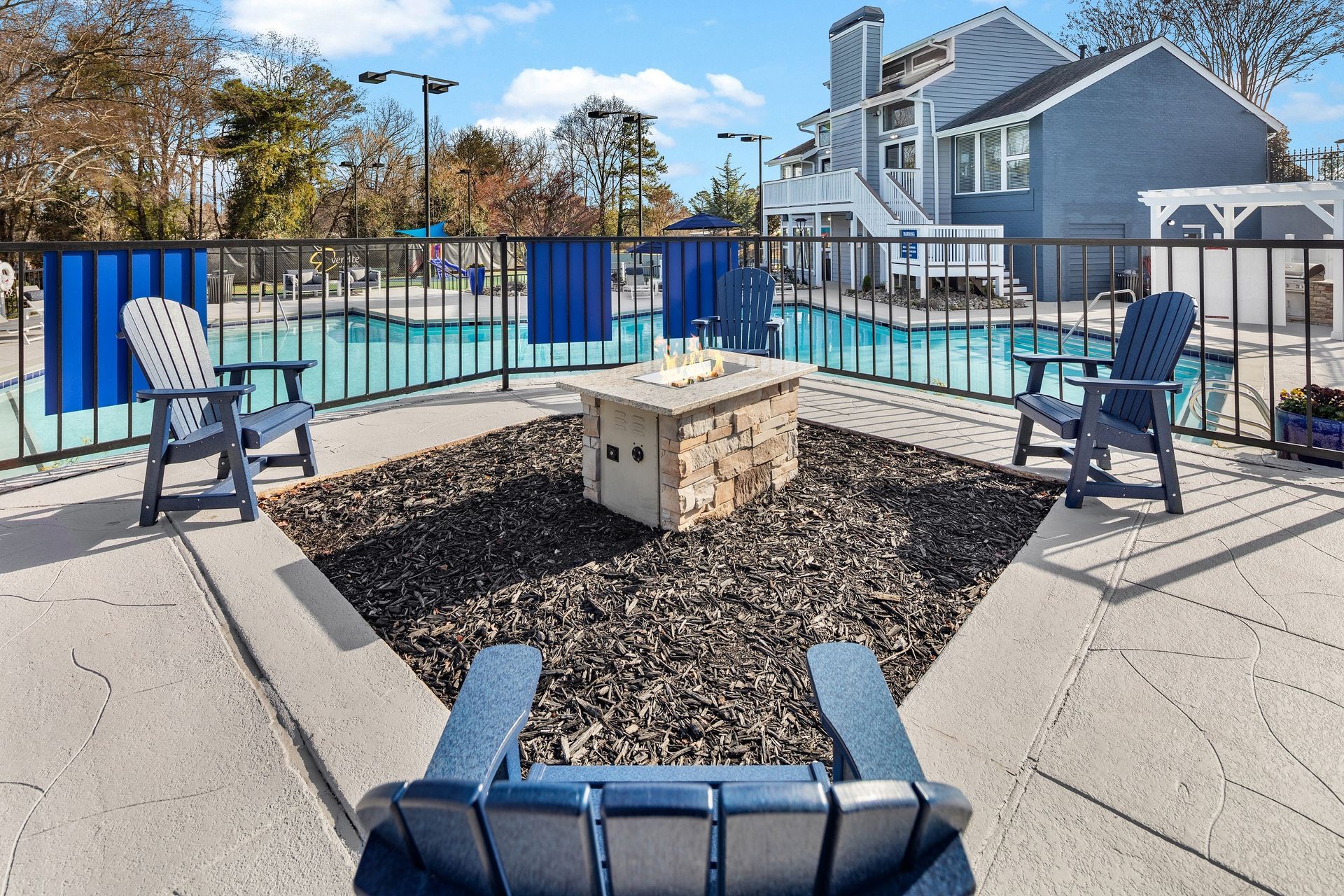Poolside seating area with fire pit and blue Adirondack chairs.