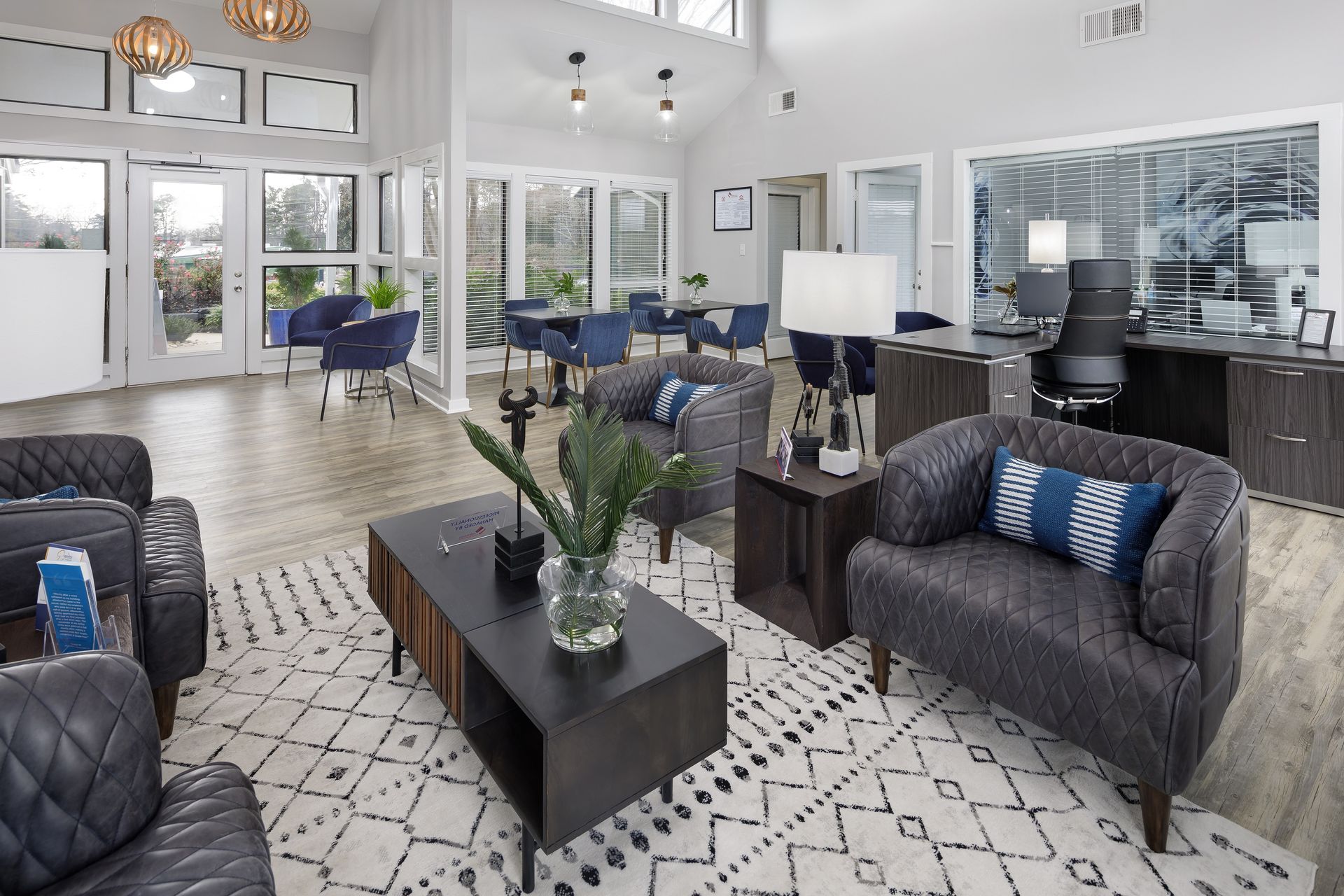 Modern lounge with armchairs, coffee table, and dining table in a bright room with large windows.