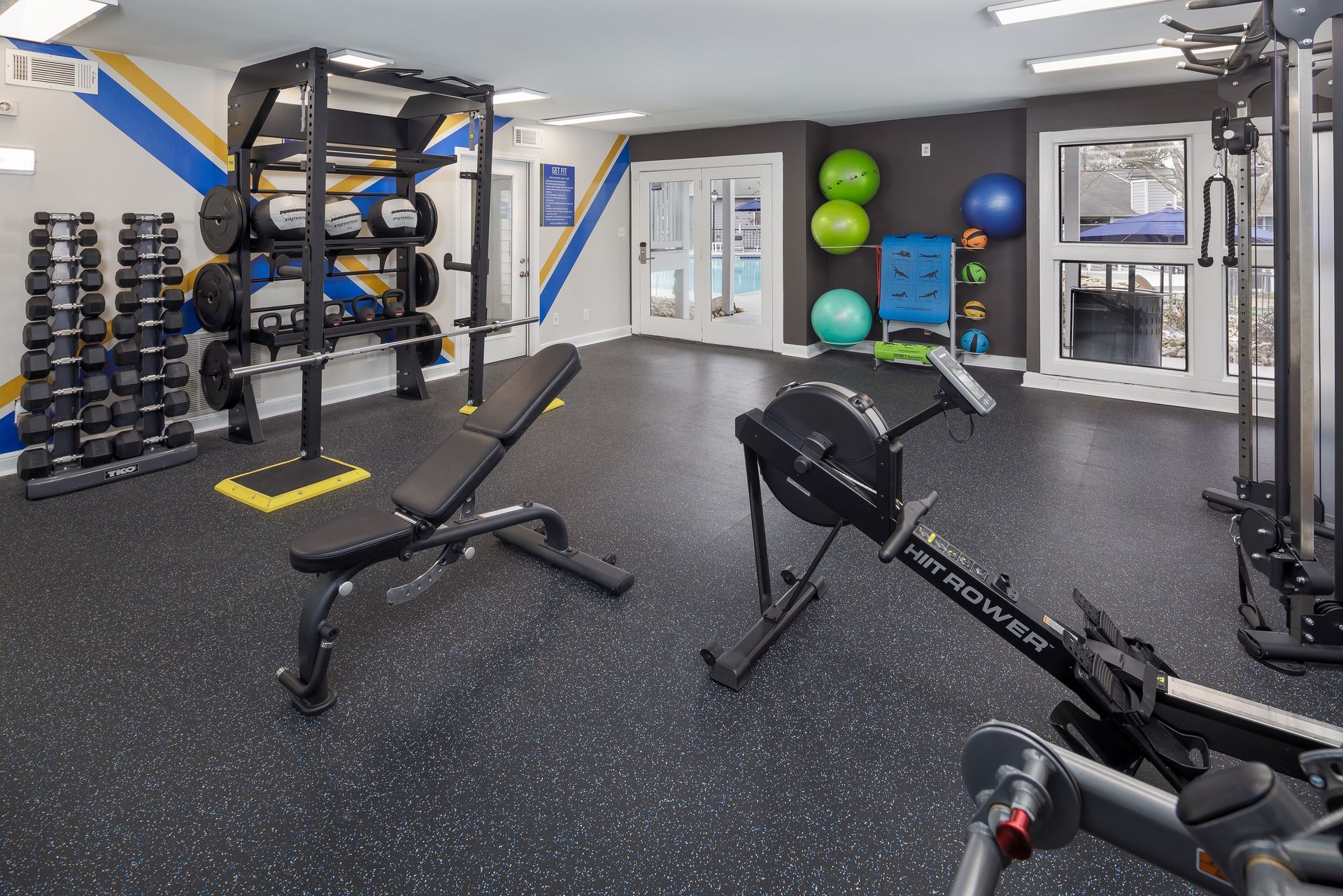 Gym interior with weights, bench, rowing machine, and exercise balls.