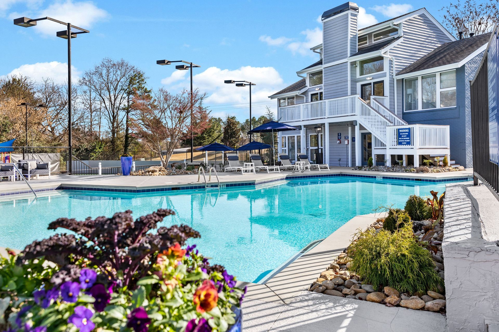 Swimming pool in front of a blue apartment building. Pansies in the foreground. Sunny day.