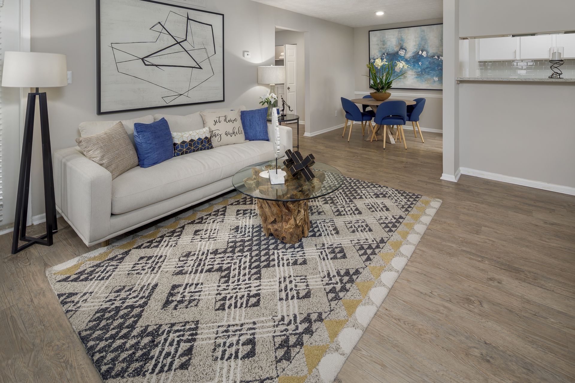 Living room with white couch, patterned rug, artwork, dining area, neutral colors.