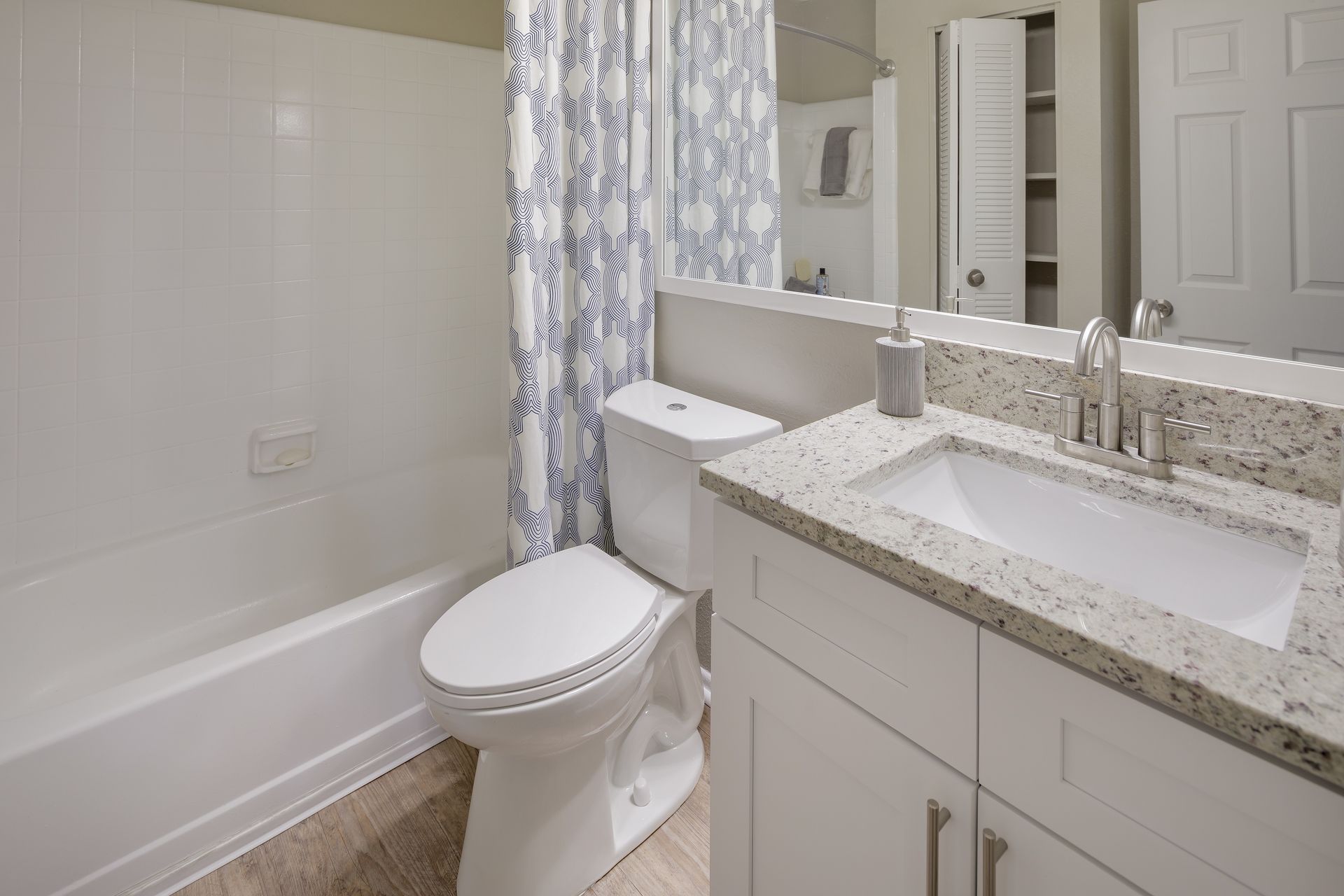 Bathroom with white tub, toilet, vanity, and floral shower curtain.