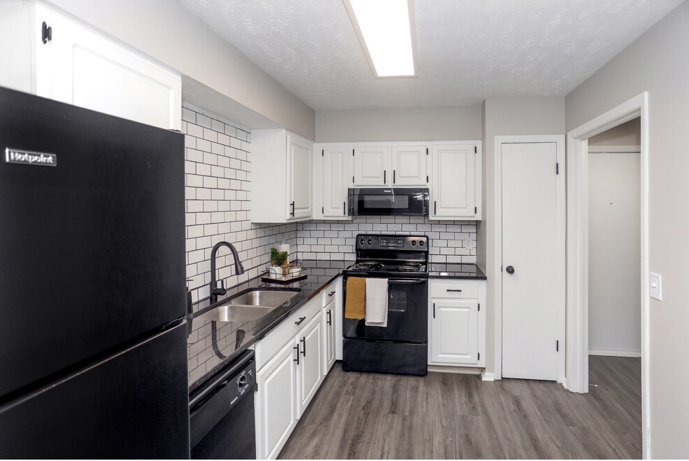 Black appliances in a white kitchen with subway tile backsplash and dark countertops.