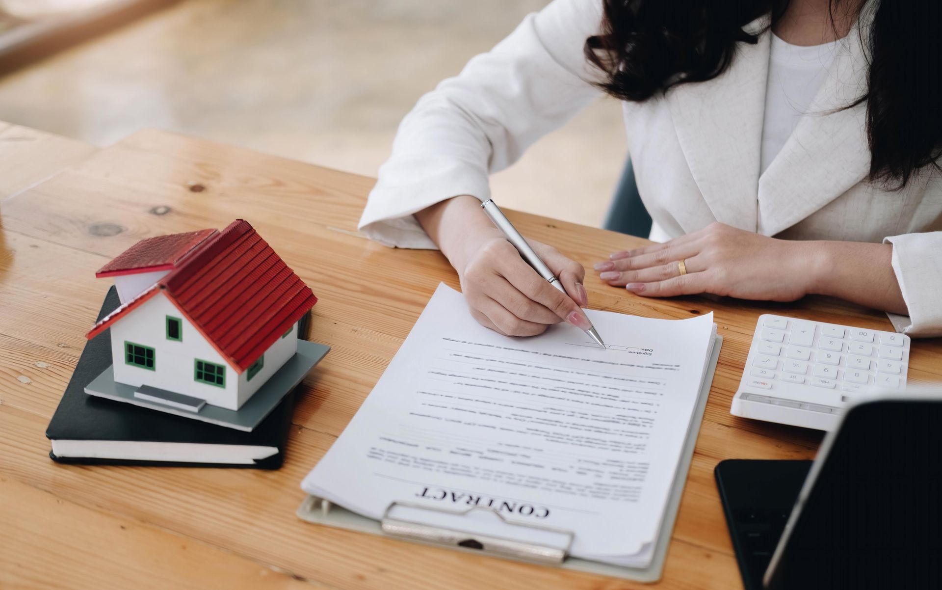 Woman signing a contract at a desk with a model house and a keyboard.