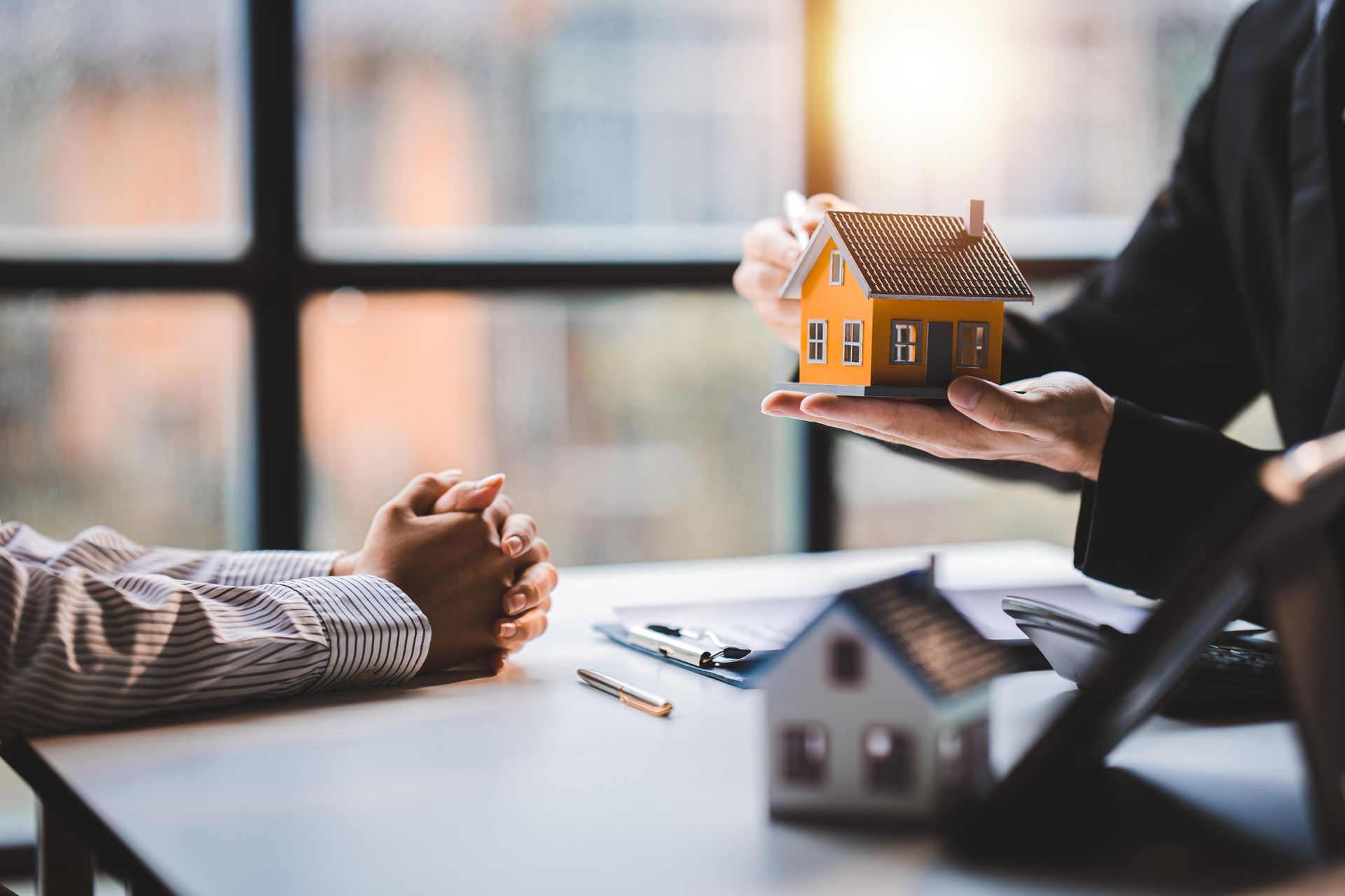 Real estate agent presenting miniature house model to a client at a desk.