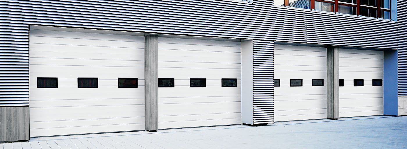 White garage doors with black windows, against a textured metal building.