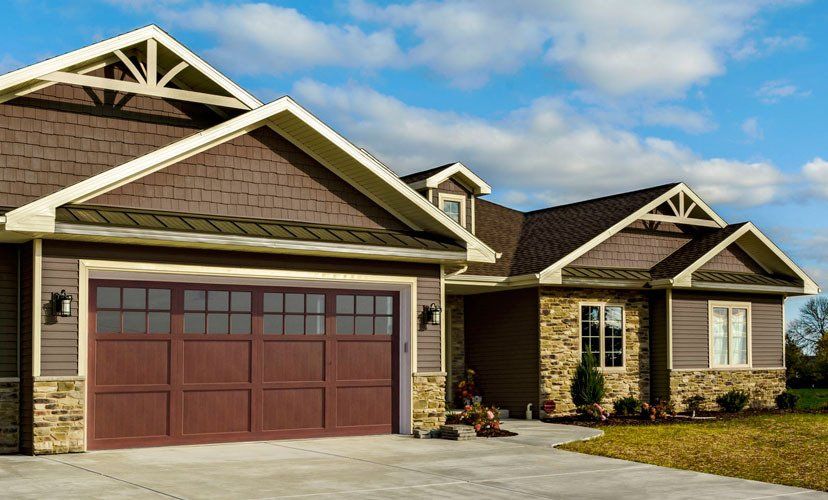 Brown house with brown garage door and stone accents against a blue sky.