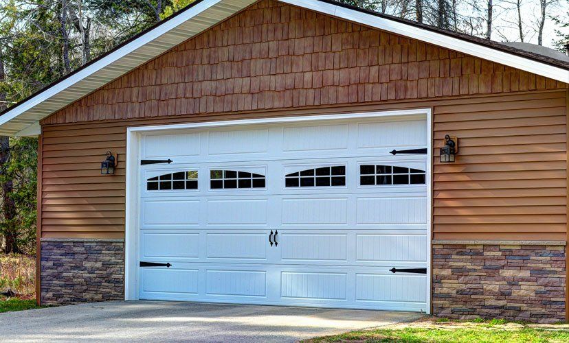White garage door on a brown sided building, with decorative black hardware.