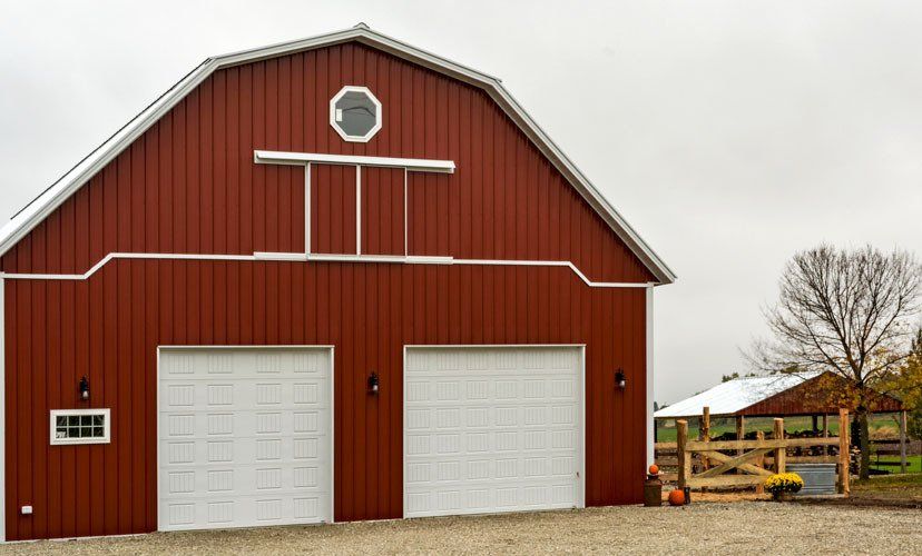 Red barn with two white garage doors, small window, and a shed in a rural setting.