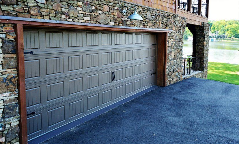 Tan garage door with brown trim set in a stone house, overlooking a lake.