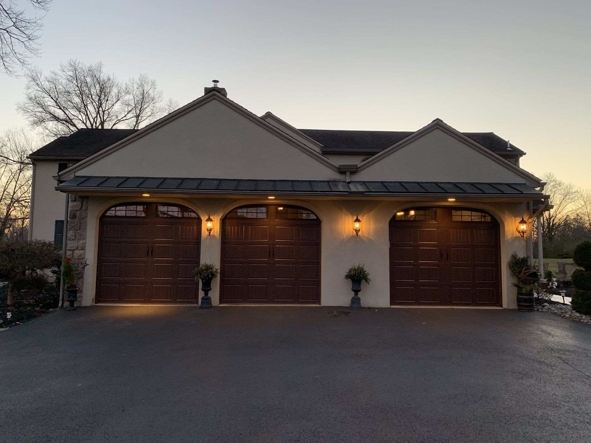 Three-car garage with brown doors and tan exterior. Dusk setting.