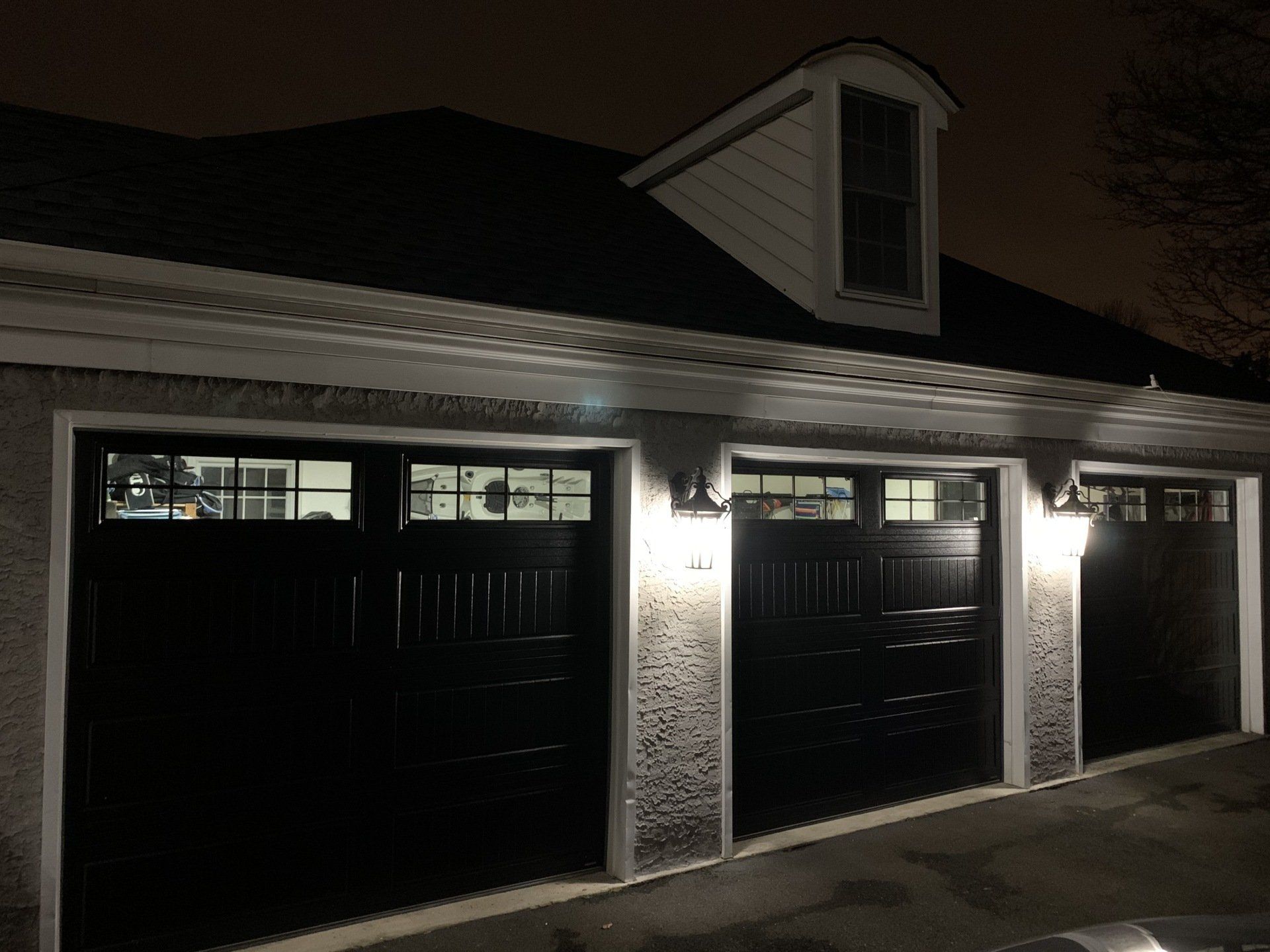 Dark garage with three closed black doors and lit wall sconces at night.