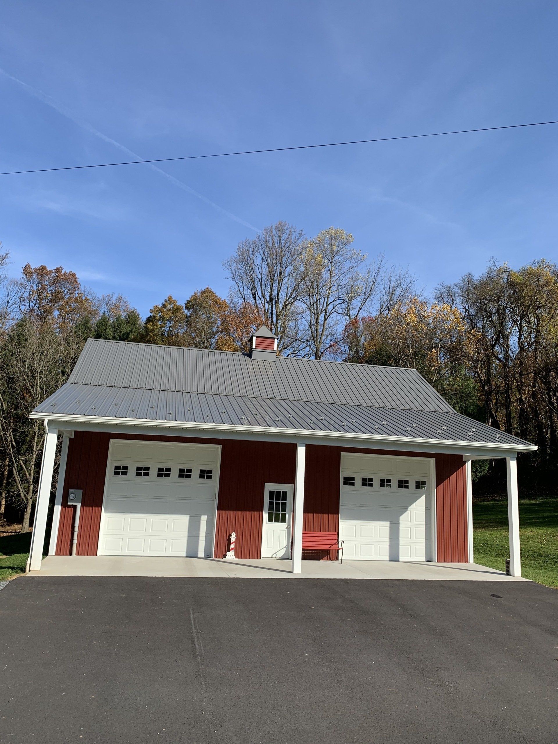 Red garage with white doors, red trim, and a dark asphalt driveway under a blue sky.