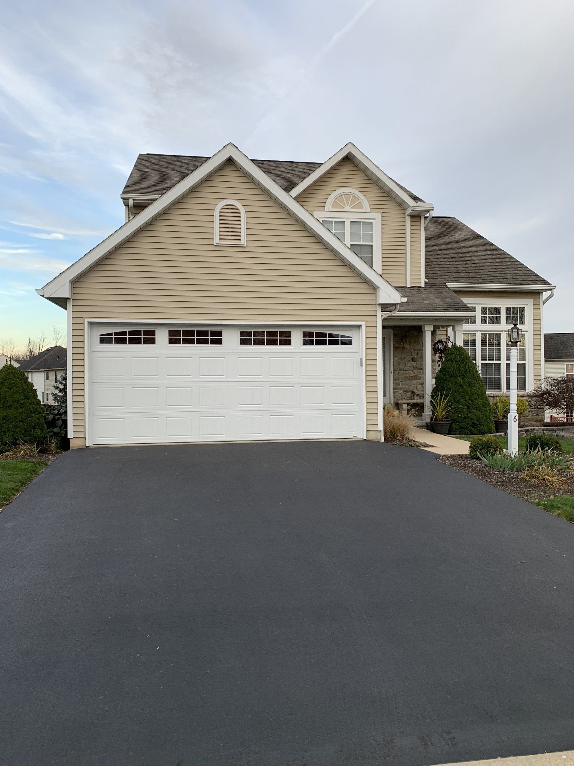 Tan house with white garage door and black asphalt driveway. Cloudy sky.
