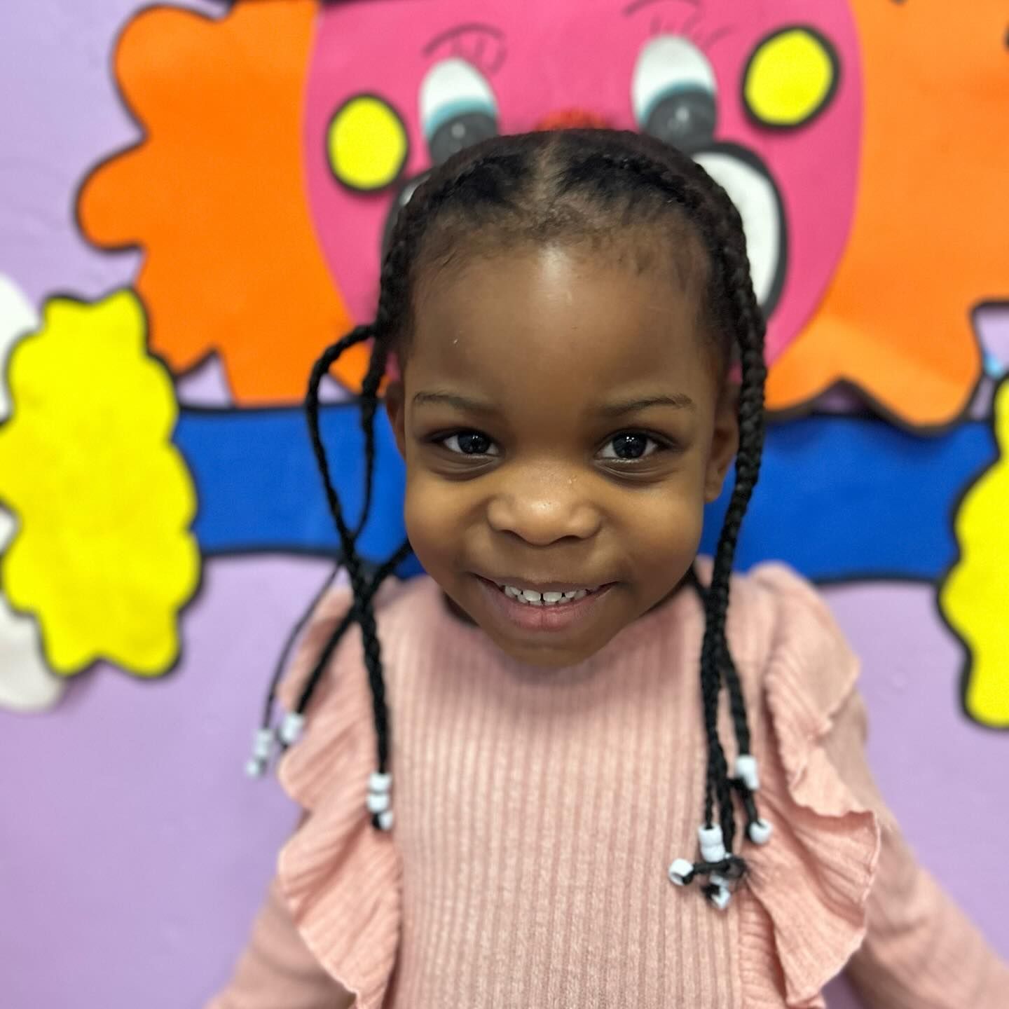 A little girl with braids is smiling in front of a cartoon face