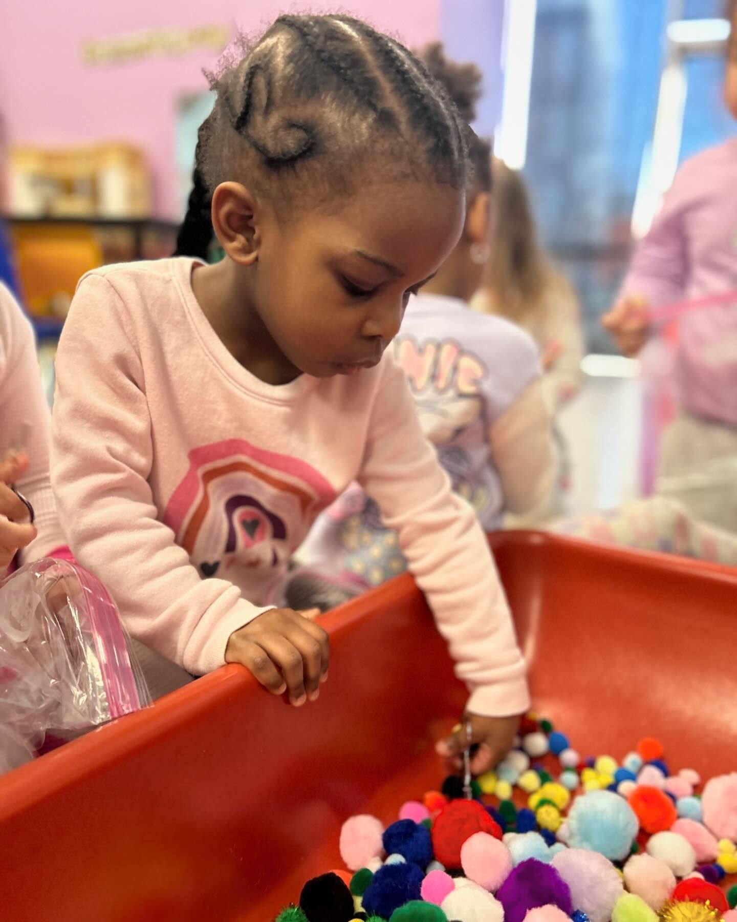 A little girl is playing with pom poms in a bin.