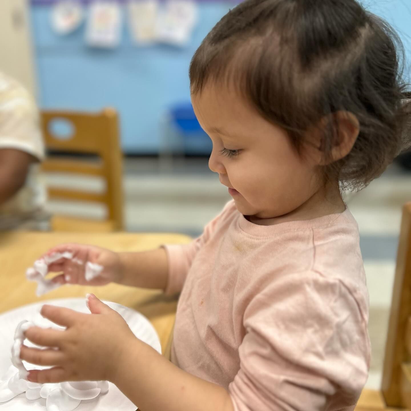 A little girl in a pink shirt is sitting at a table