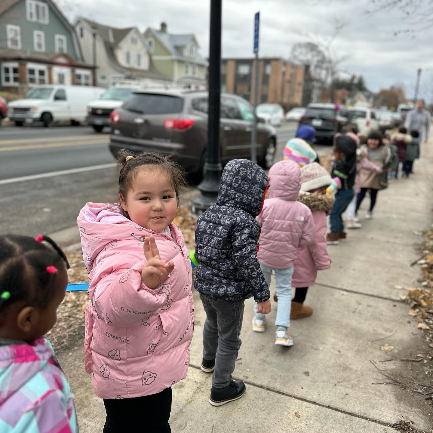 A group of children are standing in a line on a sidewalk.