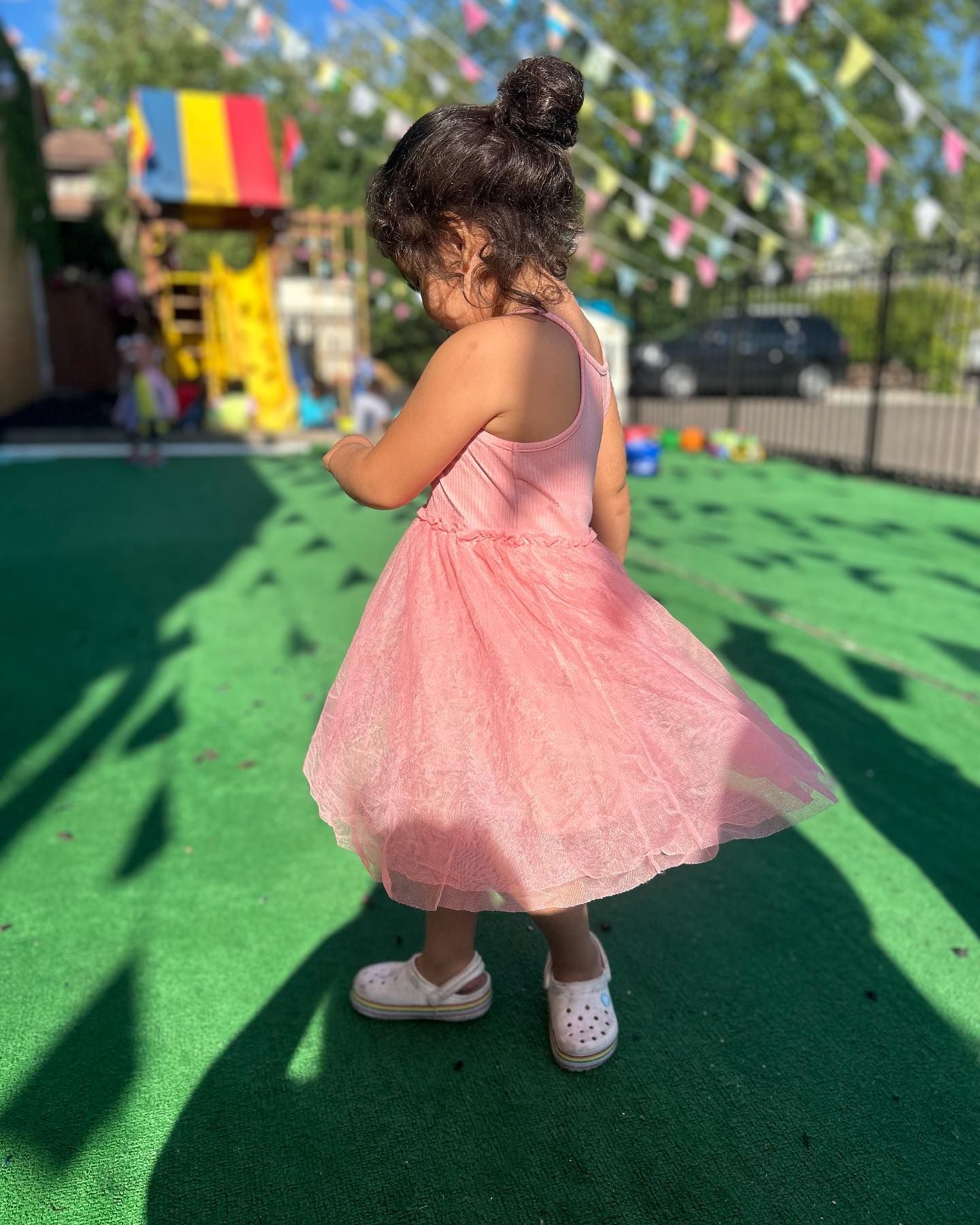 A little girl in a pink dress is standing in a playground.