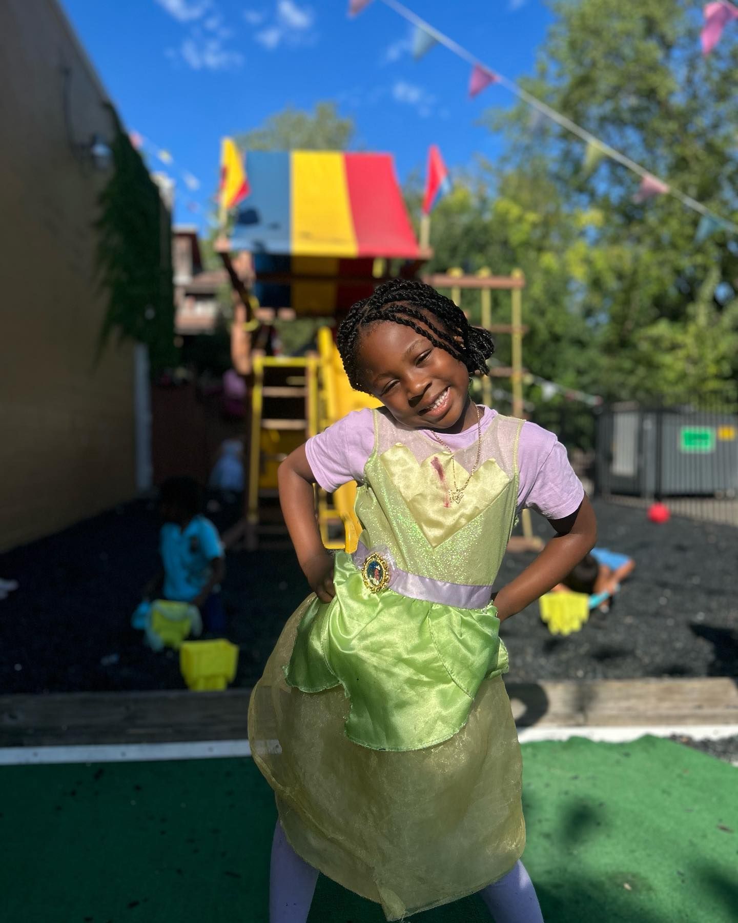 A little girl in a green dress is standing in front of a playground.