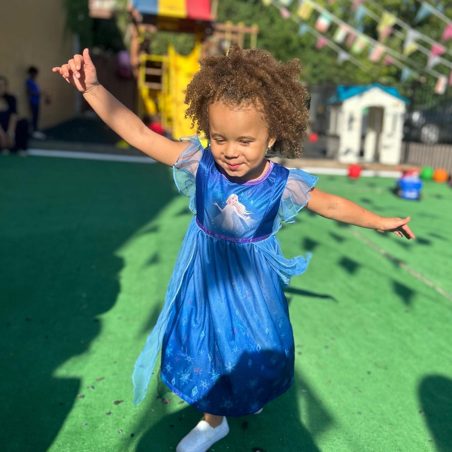 A little girl in a blue dress is dancing in a playground.