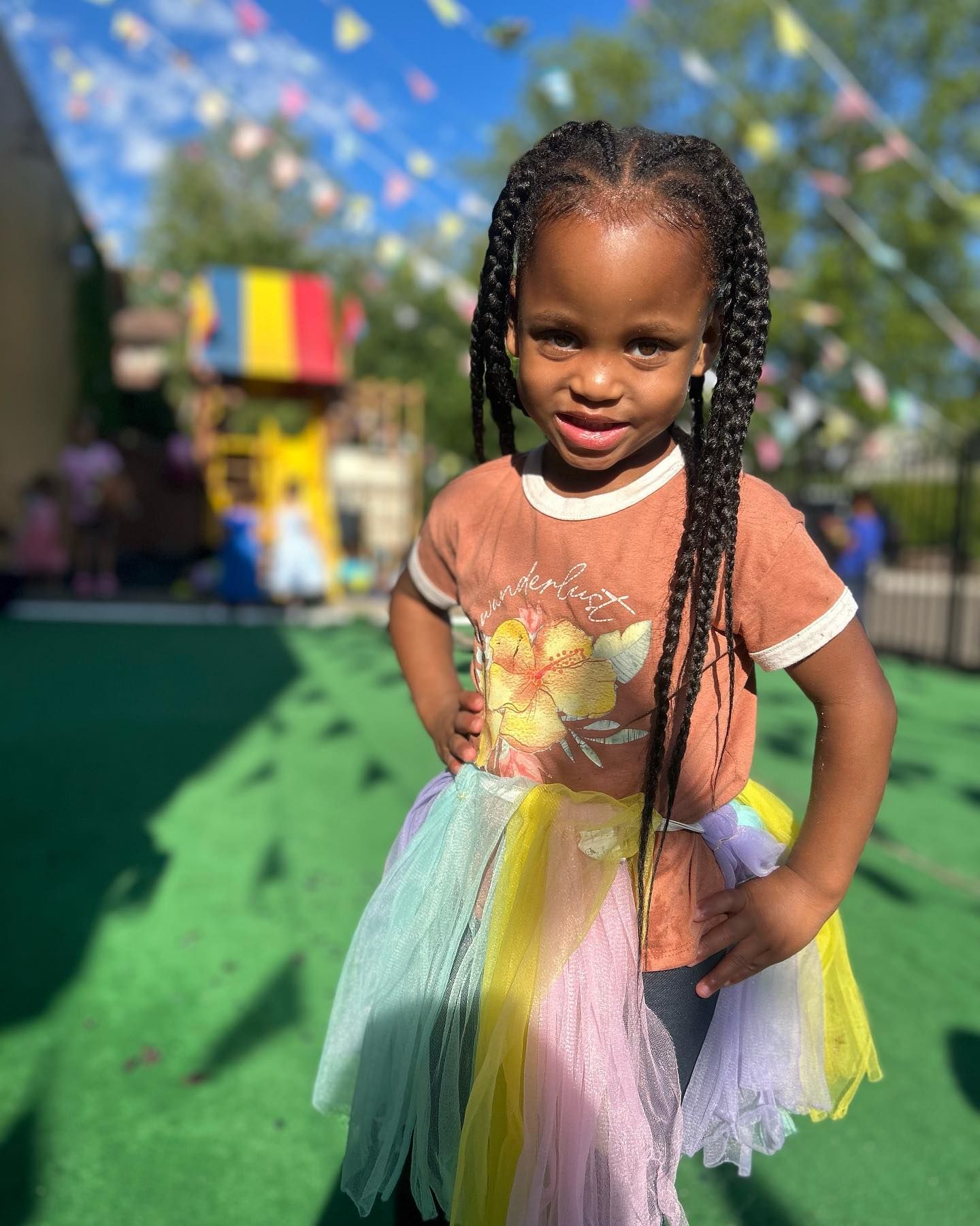 A little girl wearing a colorful tutu is standing on a green field.