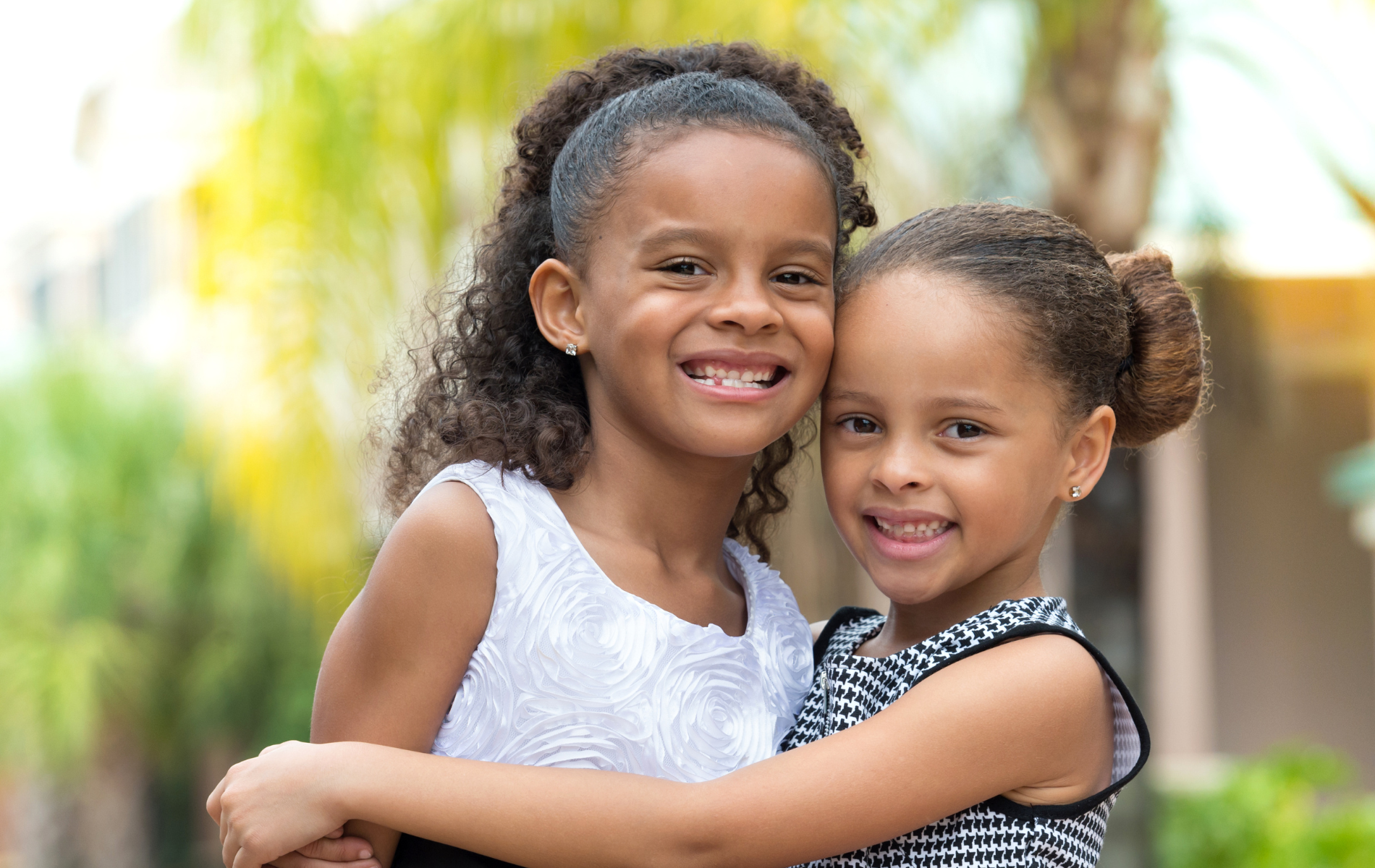 Two little girls are hugging each other and smiling for the camera.